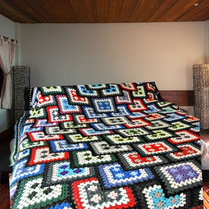 May include: A colorful crocheted blanket with a geometric pattern in shades of red, blue, green, white, and black. The blanket is spread out on a bed in a bedroom.