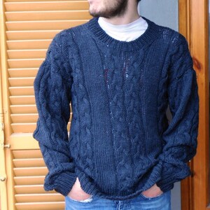 May include: A dark blue cable knit sweater with a crew neck. The sweater is made of a soft, comfortable material and has a relaxed fit.
