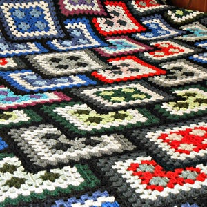 May include: A black and white crocheted blanket with a geometric pattern of squares and diamonds. The blanket features various colors, including red, blue, green, and purple.