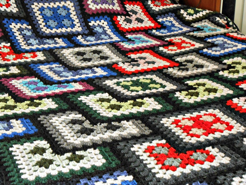 May include: A black and white crocheted blanket with a geometric pattern of squares and diamonds. The blanket features various colors, including red, blue, green, and purple.