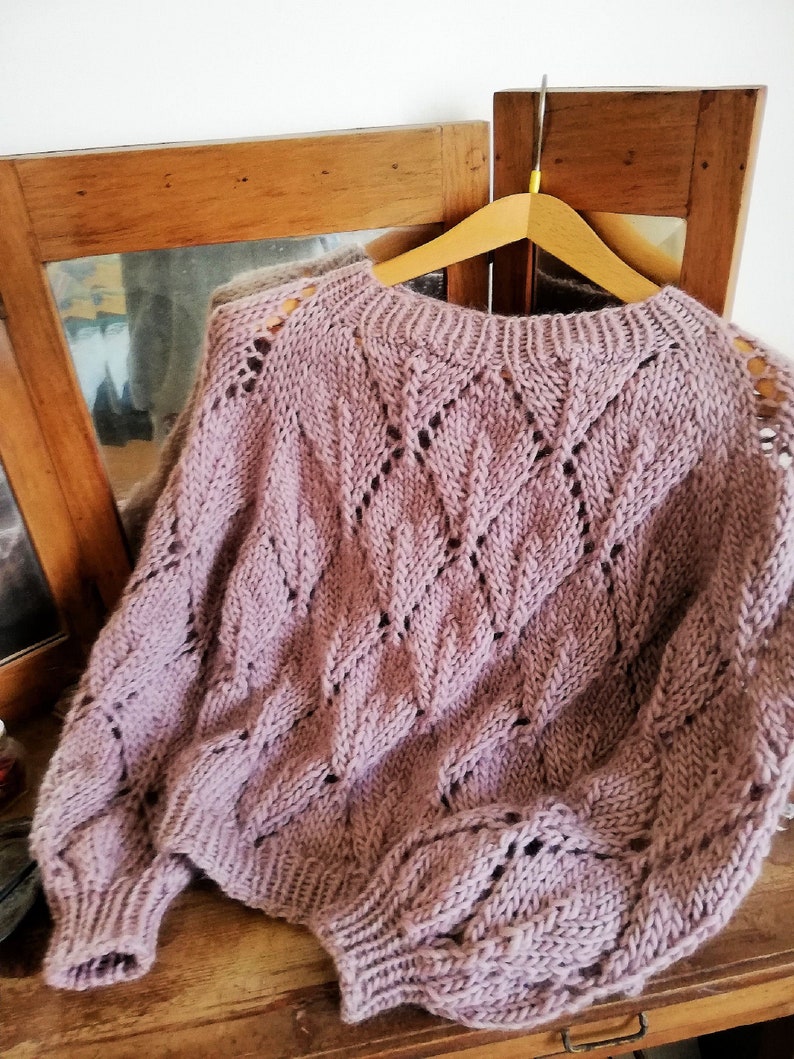 K&ouml;nnte beinhalten: Ein weicher, mauvefarbener Strickpullover mit einem zarten Lochmuster. Der Pullover hat eine lockere Passform und lange &Auml;rmel.