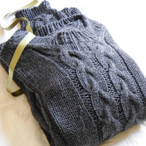 May include: A dark gray cable knit sweater with a turtleneck collar. The sweater is folded and tied with a green ribbon.