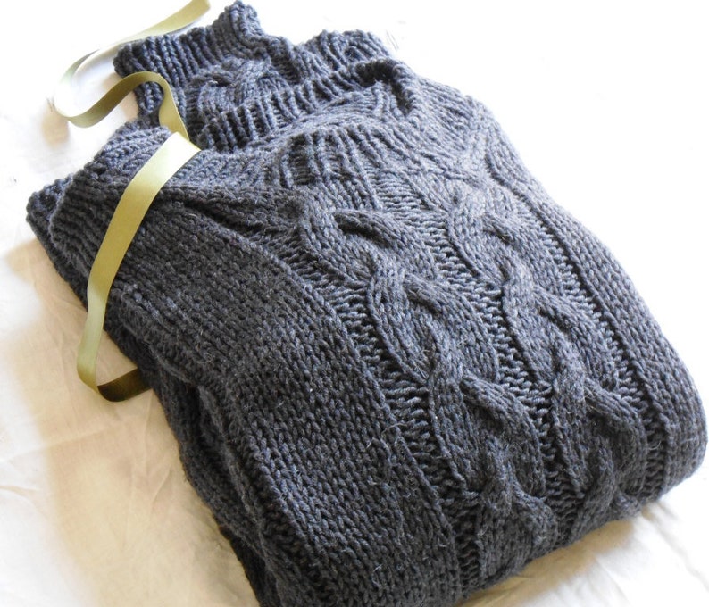 May include: A dark gray cable knit sweater with a turtleneck collar. The sweater is folded and tied with a green ribbon.
