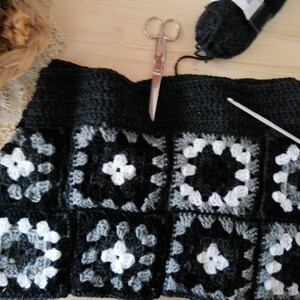 May include: A black, gray, and white crocheted square with a crochet hook and yarn.