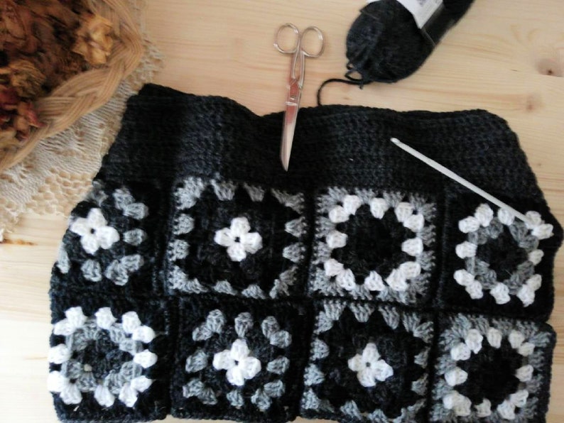 May include: A black, gray, and white crocheted square with a crochet hook and yarn.