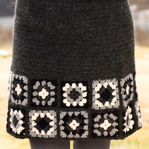 May include: A gray crochet skirt with a black, white, and gray granny square trim. The skirt is made with a textured yarn and has a simple, classic design.  DROPS DESIGN. www.GARNSTUDIO.com