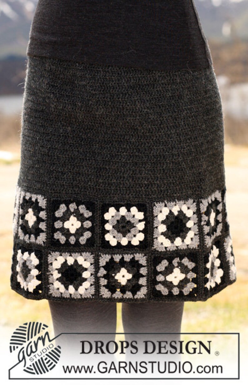 May include: A gray crochet skirt with a black, white, and gray granny square trim. The skirt is made with a textured yarn and has a simple, classic design.  DROPS DESIGN. www.GARNSTUDIO.com
