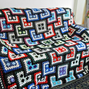 May include: A colorful crocheted throw blanket with a geometric pattern in shades of black, white, red, blue, green, and purple. The blanket is made of squares and is draped over a couch.
