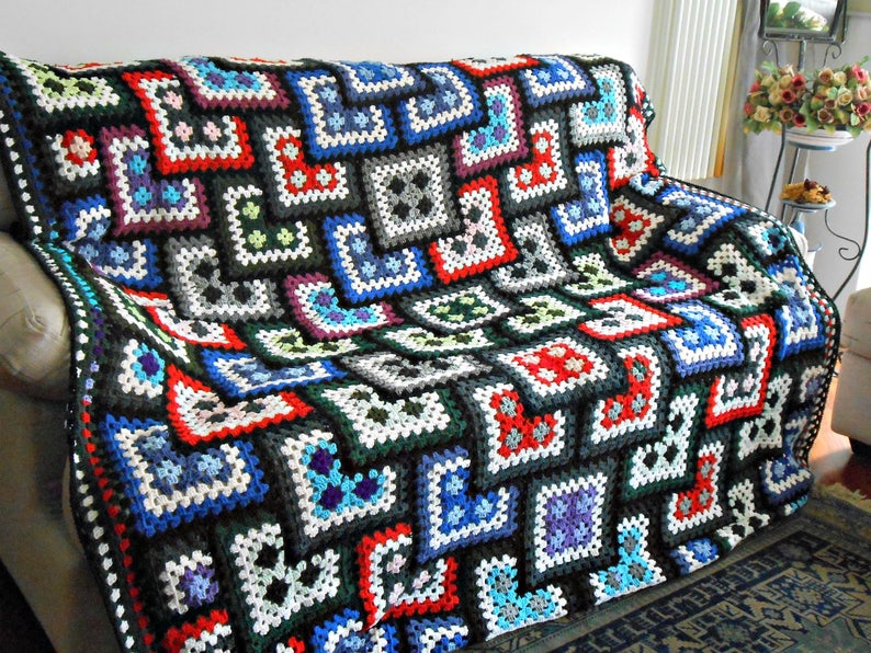 May include: A colorful crocheted throw blanket with a geometric pattern in shades of black, white, red, blue, green, and purple. The blanket is made of squares and is draped over a couch.