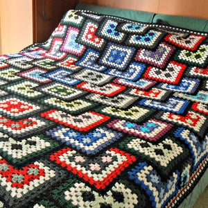 May include: A colorful crocheted blanket with a black background and a variety of squares in different colors, including red, blue, green, and white.
