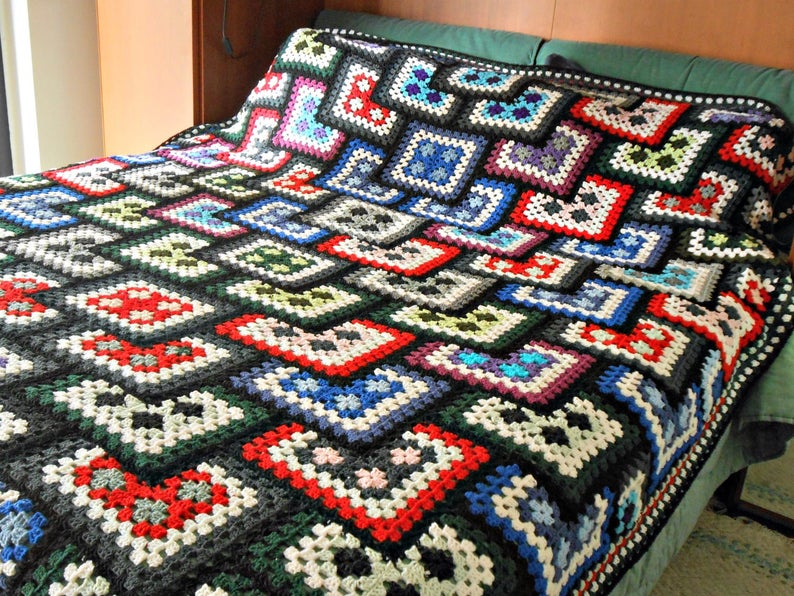 May include: A colorful crocheted blanket with a black background and a variety of squares in different colors, including red, blue, green, and white.
