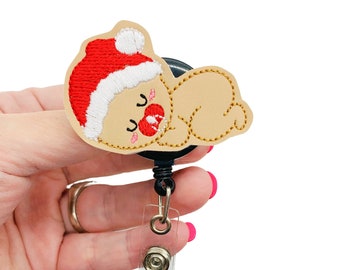 May include: A beige gingerbread person wearing a red and white Santa hat with a red candy cane in its mouth. The gingerbread person is attached to a black retractable badge reel with a clear plastic strap.
