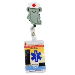 K&ouml;nnte beinhalten: Ein grauer Hammerhai, der eine rote und wei&szlig;e Krankenschwesterm&uuml;tze tr&auml;gt und einen schwarzen einziehbaren Ausweishalter mit einem wei&szlig;en Ausweis, auf dem "North Dakota Emergency Medical Services Geoffrey EMT Expires 6/30/2015" steht.