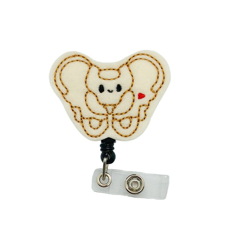 May include: A white felt badge reel with a cute embroidered design of a pelvis bone with a small red heart. The reel has a black retractable cord and a clear plastic clip.