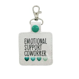 May include: White keychain with a silver clip and a green button. The keychain has the text "Emotional Support Coworker" and three green hearts.