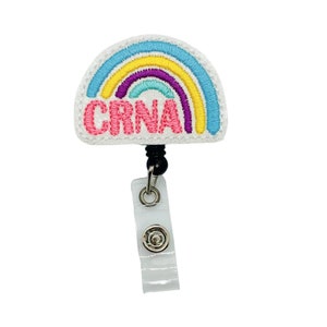 May include: A white rainbow-shaped badge holder with the text "CRNA" in pink letters. The rainbow has yellow, purple, blue, and turquoise stripes. The badge holder is attached to a black retractable badge reel.