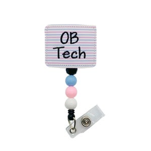 May include: A white and pink striped badge holder with the text "OB Tech" in black. The holder is attached to a retractable badge reel with blue, pink, and white beads.