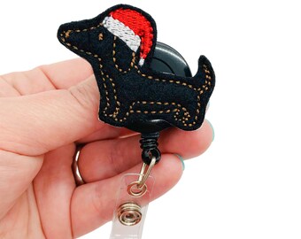 May include: Black felt dog with a red and white Santa hat, attached to a black retractable badge reel with a clear plastic clip.