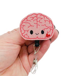May include: Pink glitter brain with a red heart and a black retractable badge reel.