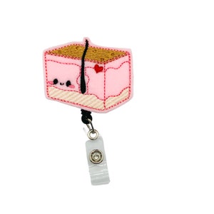 May include: A pink and brown cartoon skin cell with a black hair follicle and a red heart. The cell is attached to a black retractable badge reel with a clear plastic badge holder.