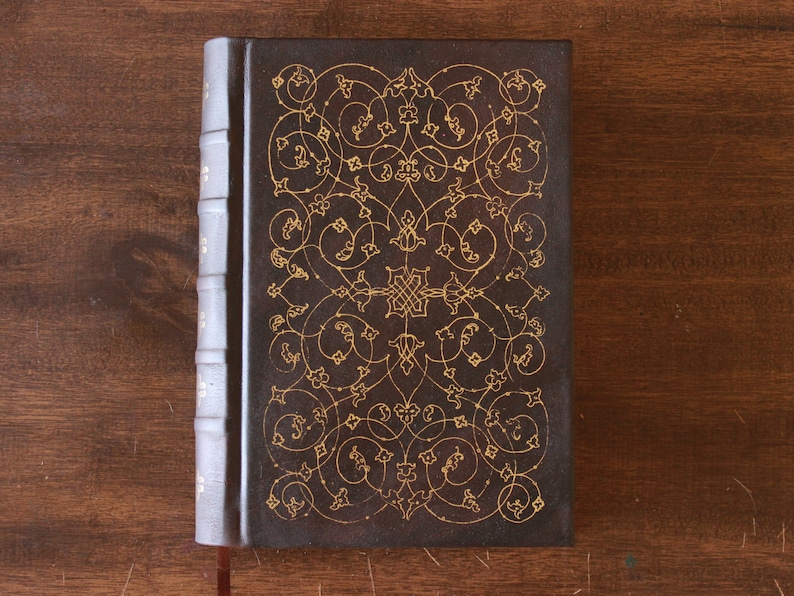 K&ouml;nnte beinhalten: Ein dunkelbraunes, ledergebundenes Tagebuch mit einem aufwendigen goldenen Blumendesign auf dem Einband.
