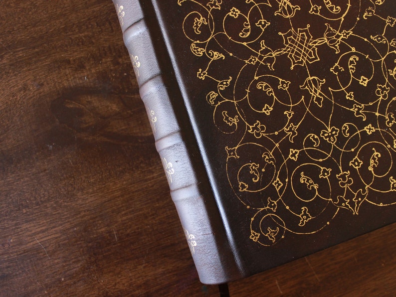 K&ouml;nnte beinhalten: Ein dunkelbraunes, ledergebundenes Buch mit goldenen, filigranen Blumenmustern auf dem Einband.
