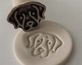 Może przedstawiać: Ceramiczna pieczątka z psem z drewnianym uchwytem, obok pasującego odcisku. Pieczątka przedstawia szczegółowy kontur pyska psa. Pieczątka i odcisk są w odcieniach brązu i kremu.