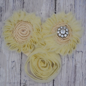 May include: Three yellow fabric flowers with a single rhinestone button in the center of one flower.