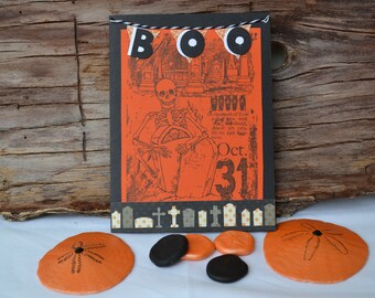 May include: A Halloween card with a black and white illustration of a skeleton holding a tombstone. The card has a banner that says "BOO" with black and white circles. The card also has the text "Oct. 31" on it.