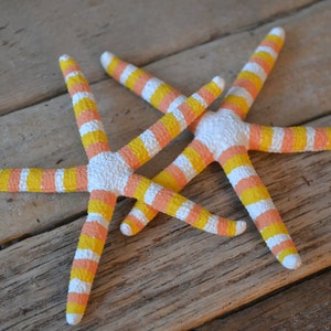 May include: Two starfish painted with white and yellow stripes. The starfish are arranged in a cross pattern on a wooden surface.