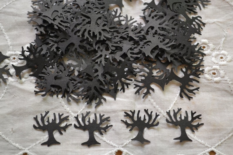 May include: A pile of black paper cutouts of trees, scattered on a white lace tablecloth. There are four larger trees in the bottom of the image.