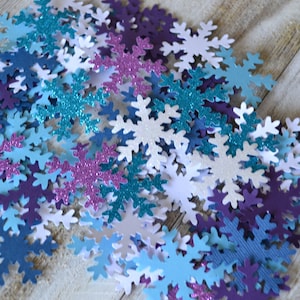 May include: A collection of snowflake-shaped paper cutouts in various shades of blue, purple, and white. Some of the snowflakes have glitter.
