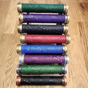 May include: A collection of eight cylindrical objects with textured surfaces in various colors, including green, purple, black, red, blue, and copper. Each cylinder has brass or copper-colored metal ends.