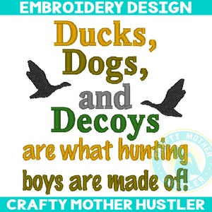 Puede incluir: Diseño de bordado con el texto "Ducks, Dogs, and Decoys are what hunting boys are made of!" en verde, amarillo y gris. El diseño también incluye dos siluetas grises de patos.