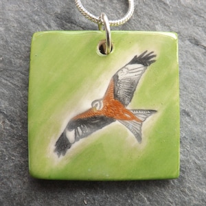 Handmade Ceramic Red Kite Pendant, striking green grass background, bird lover gift