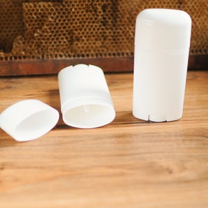 May include: Three white deodorant containers, two are open and one is closed. The containers are on a wooden surface.