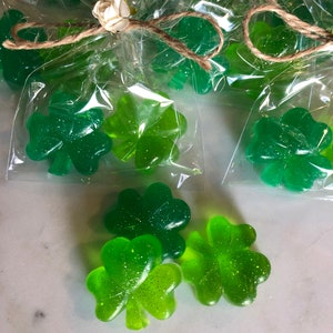 May include: Green glitter shamrock shaped soaps wrapped in clear cellophane bags tied with twine and a white flower.
