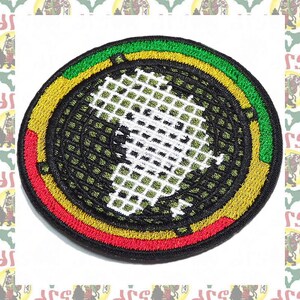 May include: A round, black embroidered patch with a white outline of the continent of Africa. The patch has a green, yellow, and red border.