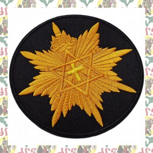 May include: A circular black patch featuring a gold starburst design with a central star and crown. The starburst has detailed wing-like elements and a yellow cross. The patch is likely an emblem or decorative element.