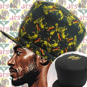 May include: Black hat with a flat brim, featuring a repeating pattern of yellow lions and red, yellow, and green flags. The hat has a structured crown and a curved brim. The design is set against a black background.