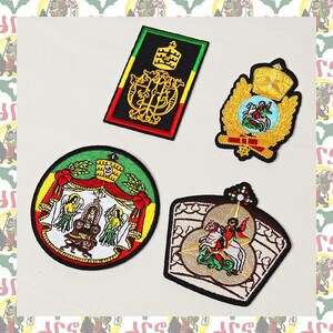 Puede incluir: Cuatro parches bordados que representan el escudo de armas imperial etíope. Los parches son de varios colores, incluyendo rojo, amarillo, verde y negro. Los parches son todos de forma circular u ovalada y presentan diseños intrincados.