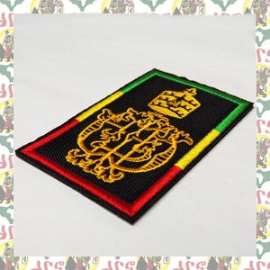 Könnte beinhalten: Ein schwarzer gestickter Aufnäher mit einem goldenen Design einer Krone und einem Symbol. Der Aufnäher ist von einem roten, gelben und grünen Rand umgeben.