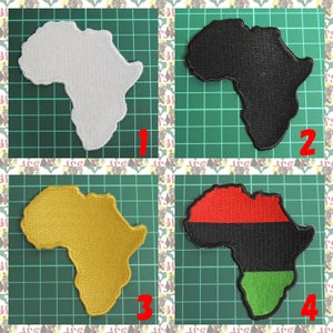 May include: Four embroidered patches shaped like the continent of Africa. The patches are white, black, yellow, and red, black, and green. The patches are on a green grid background.