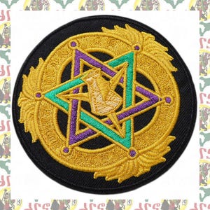 May include: Embroidered patch featuring a gold-colored star within a circle, with purple and teal accents. The patch is on a black background. The design includes a central symbol and ornate detailing.