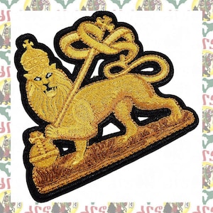 May include: An embroidered patch featuring a golden lion standing on a base, wearing a crown, and holding a tall staff topped with a cross. The design is outlined in black thread, showcasing detailed stitching of the lion's mane and body.