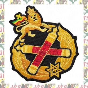May include: An embroidered patch featuring a golden lion wearing a crown and holding a flag with green, yellow, and red stripes. Below the lion are two crossed golden batons with red centers, framed by golden laurel leaves and a six-pointed star.