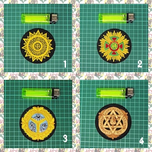 May include: Four embroidered patches with different designs. The patches are circular and feature intricate patterns in gold, red, green, and black. Each patch is displayed on a green cutting mat with a green lighter for scale.