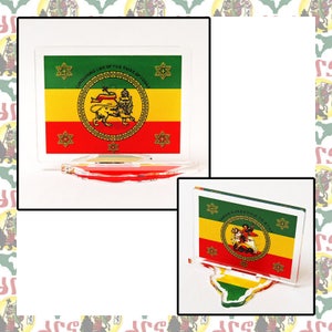 Peut inclure: Deux supports en acrylique avec un drapeau éthiopien rouge, jaune et vert imprimé dessus. Les drapeaux représentent un lion avec une couronne et le texte "CORDOVEANG EOD OF THE TRIBE OF JUDAH".