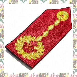 May include: A red embroidered shoulder patch with a gold wreath, cross, and chain. The patch has a black border.