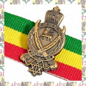 May include: A gold-colored metal pin with a lion and a crown, surrounded by swords and a star. The pin is on top of a red, yellow, and green striped ribbon.
